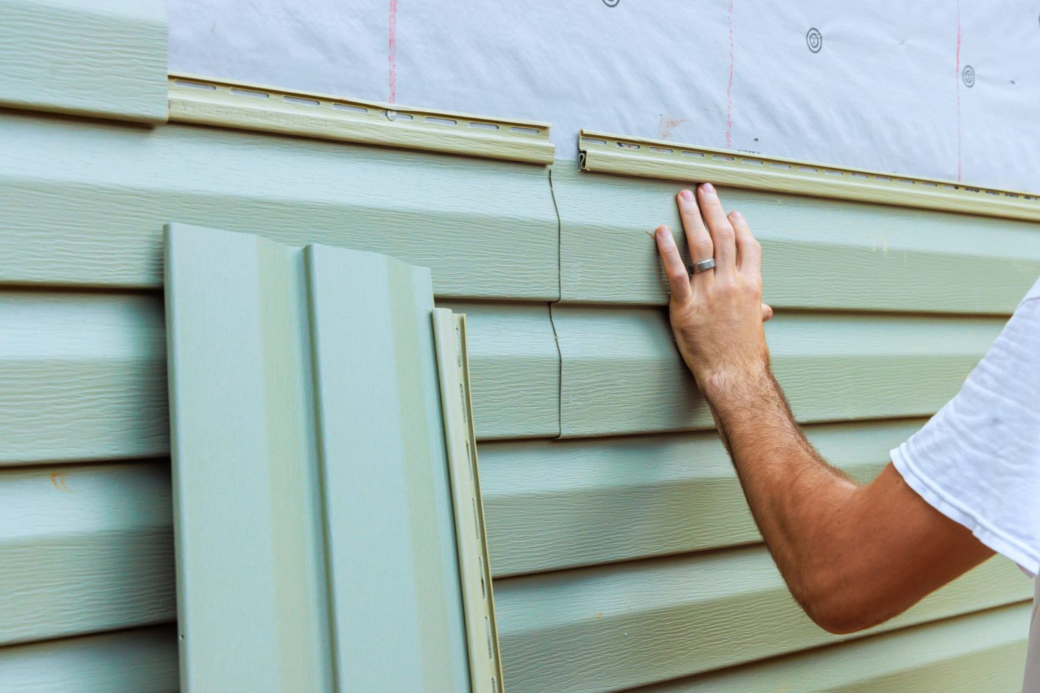 Construction worker carefully aligns, secures new vinyl siding panels on to exterior wall of new house